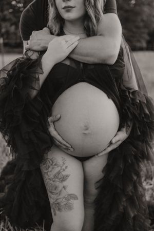 Intimate black and white maternity photo showcasing pregnancy in dramatic feathered dress.