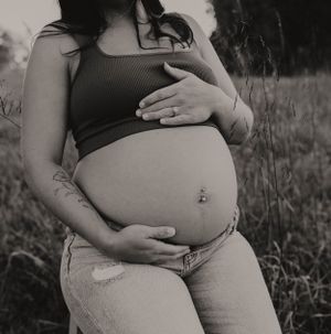 Black and white artistic maternity photo showing pregnant belly in natural setting.