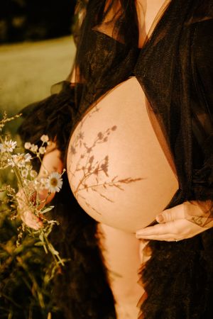 Artistic maternity photo showing shadow of flowers cast on pregnant belly in golden light.