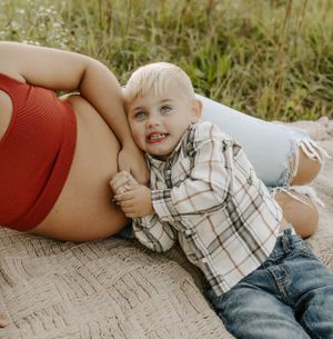 A joyful moment captured during a maternity photo session on a picnic blanket in a field.