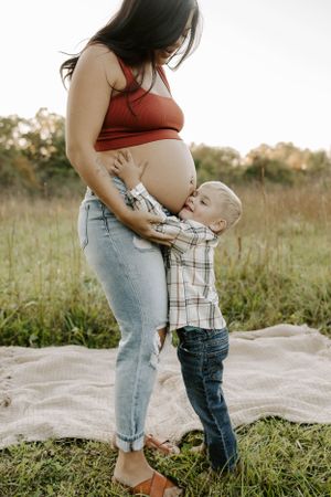 Tender moment between young child and pregnant mother in casual outdoor setting.