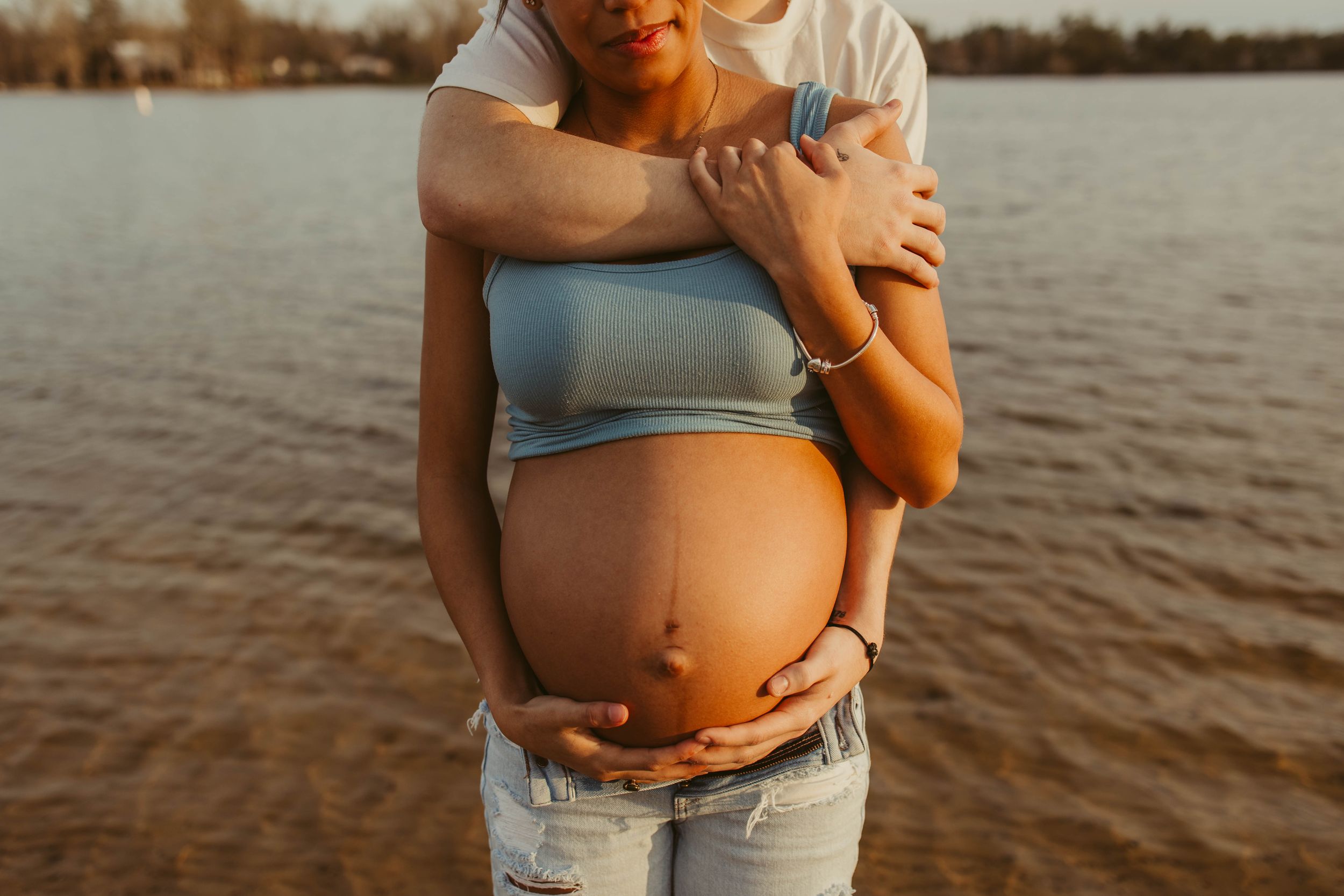 A sunset maternity photo showing loving hands embracing a pregnant belly by the water.