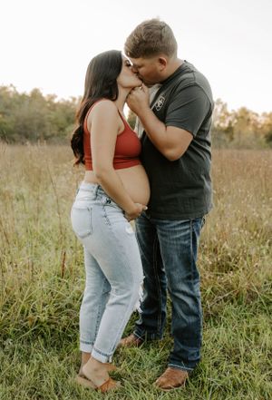 A maternity photo shoot in a golden field shows a tender moment between a couple during sunset.