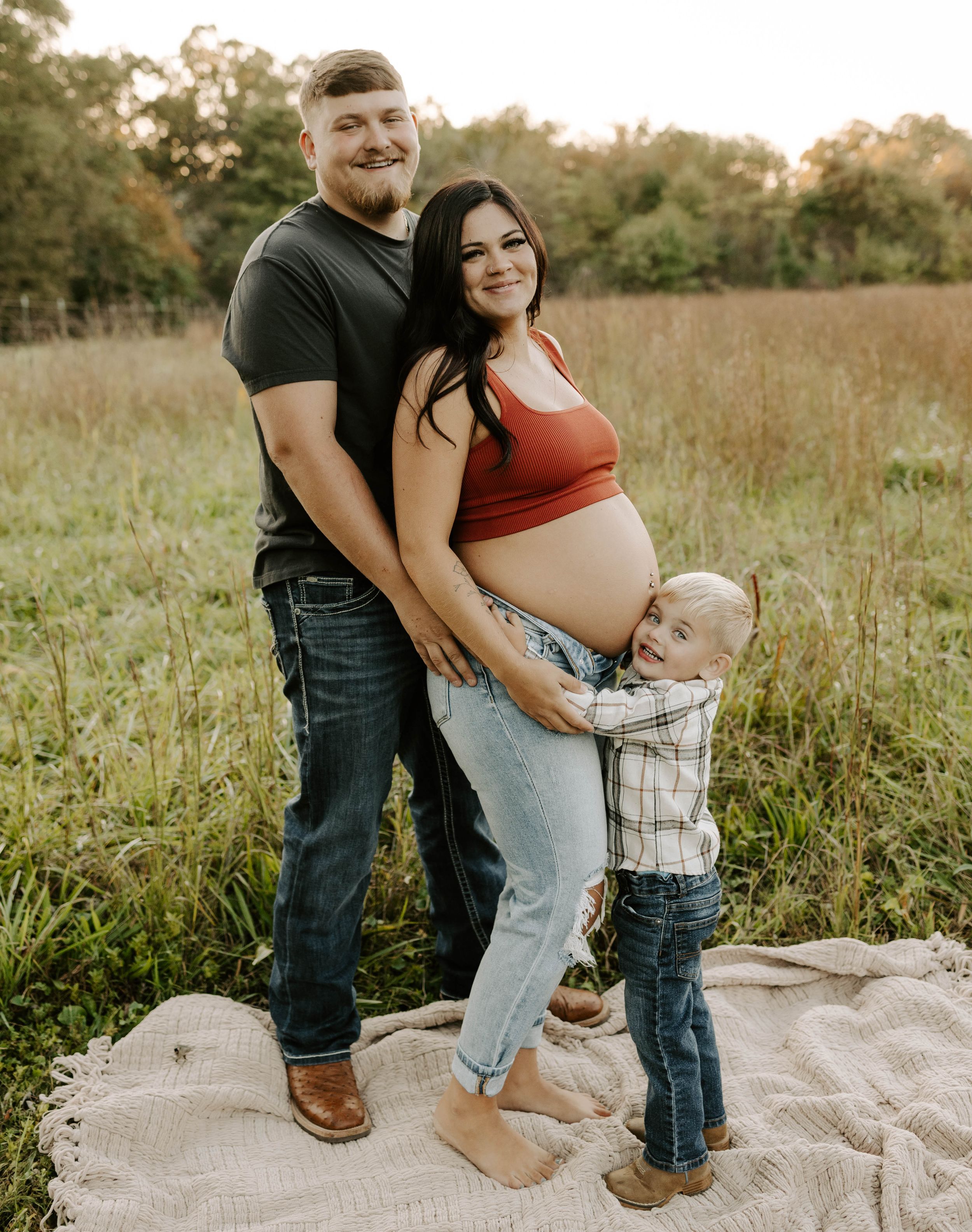 A family maternity photo shows a loving moment together in a golden field at sunset.