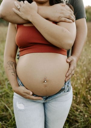 Close-up portrait of pregnant belly with hands tenderly embracing in outdoor setting.