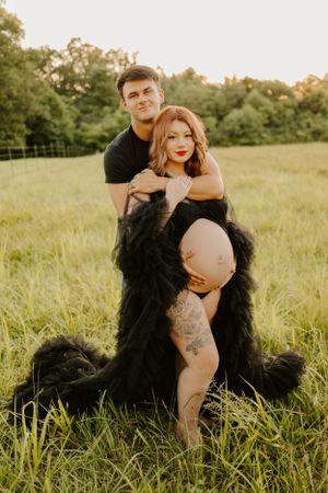 Romantic maternity photoshoot in a grassy field with dramatic black feathered dress.