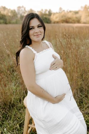 Radiant pregnant woman in white dress poses in field during golden hour.