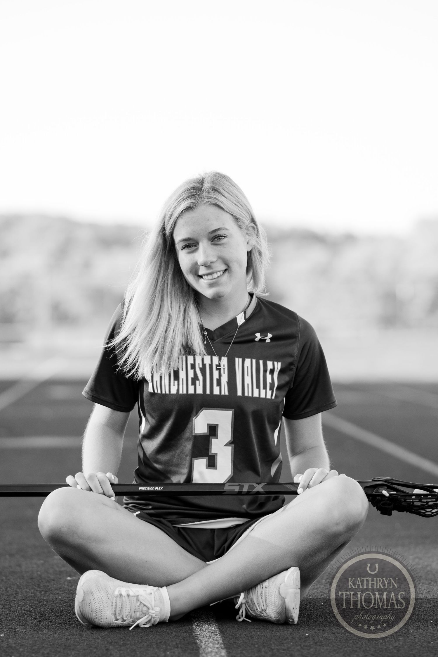 Black and white seated portrait with lacrosse sticks on sports field.