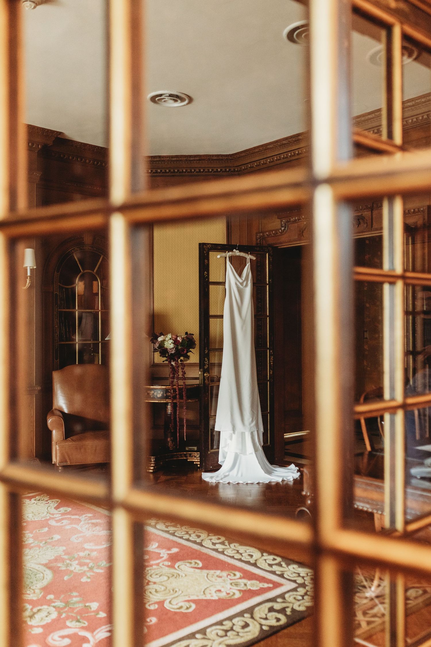 A wedding dress viewed through window panes in an elegantly furnished room.