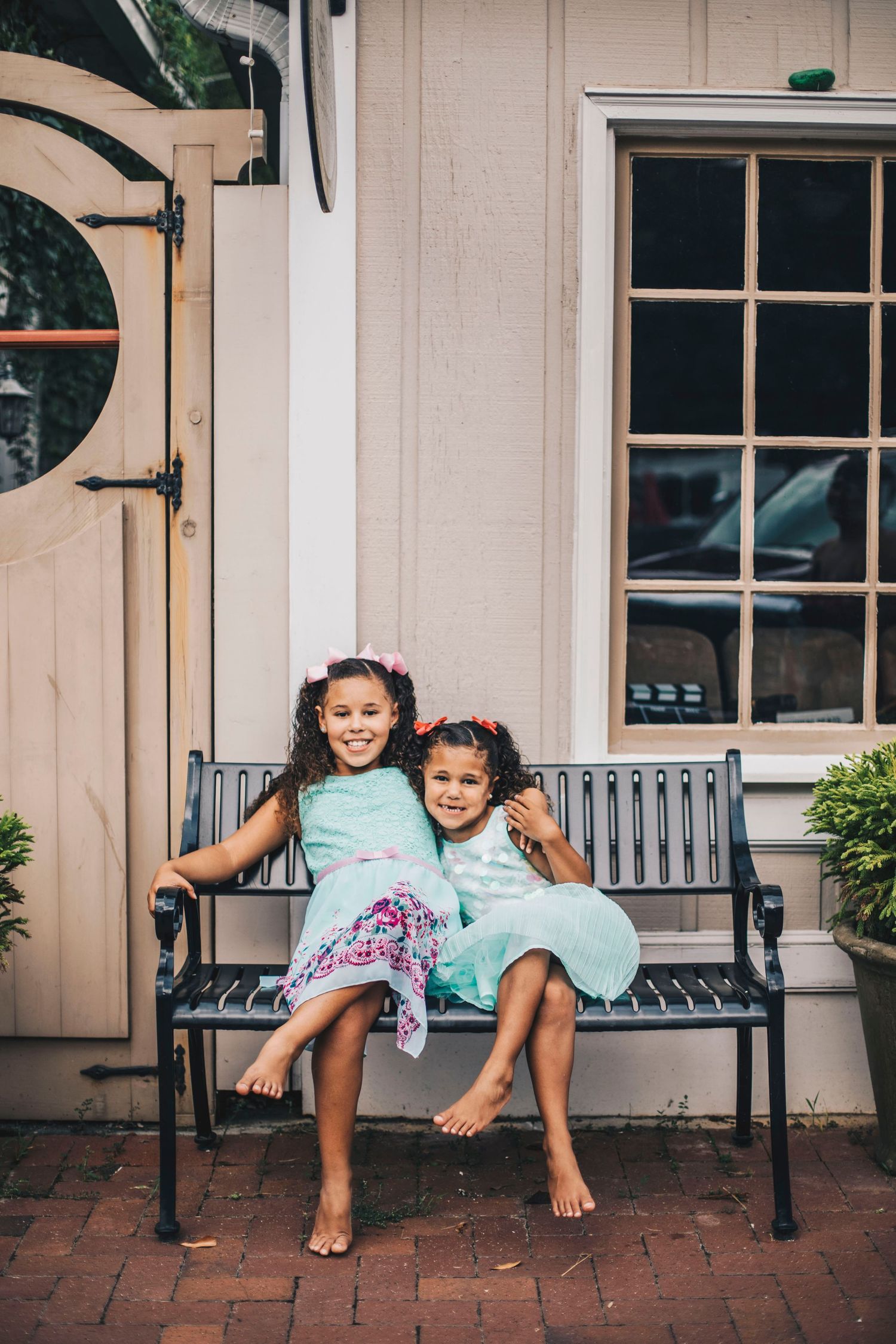 Two young girls in matching mint dresses sitting together on a bench outside a building.