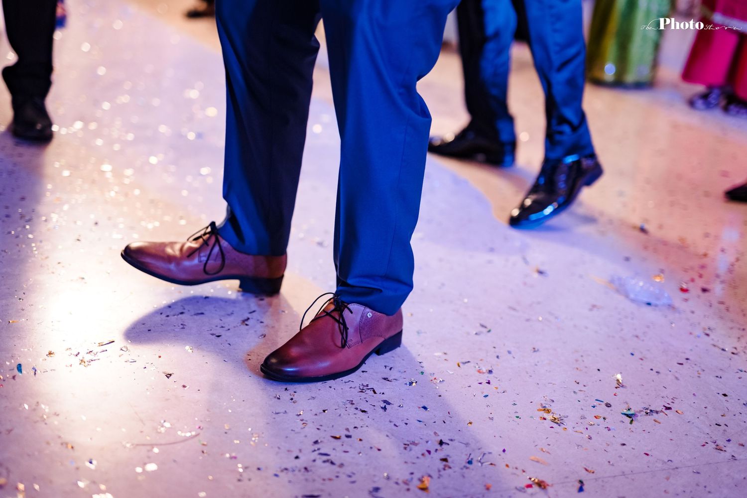 Close-up of dancing feet and formal shoes on confetti-covered reception floor.