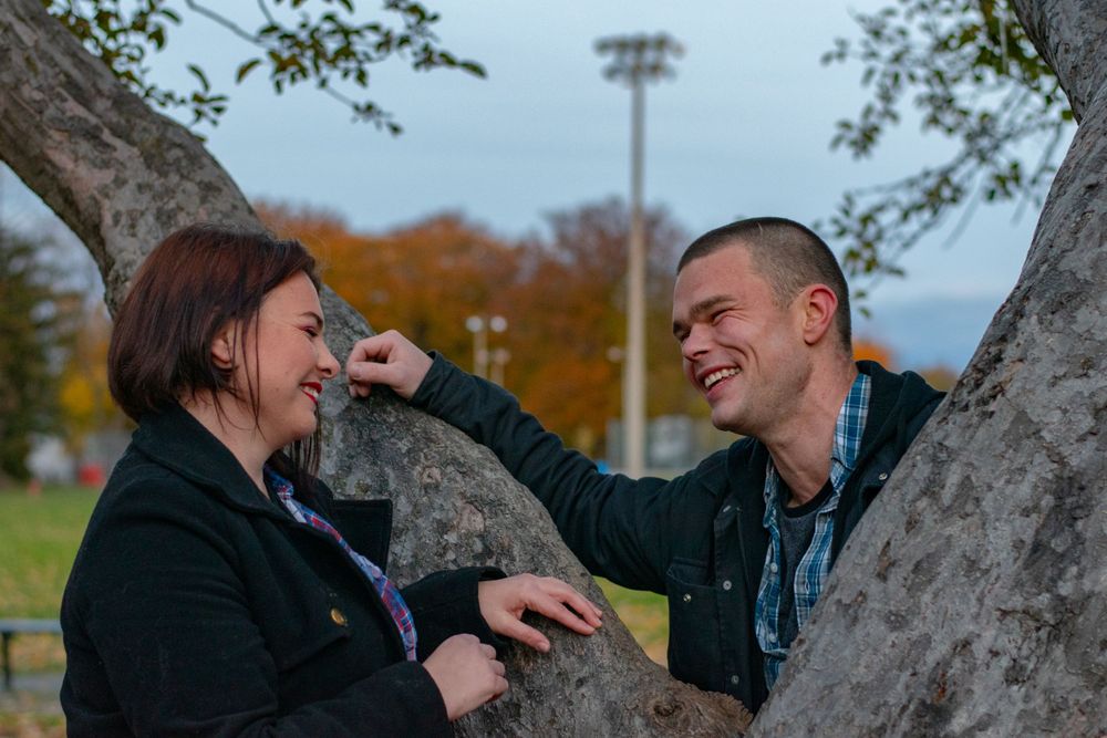 A couple smiling at each other from across a tree branch