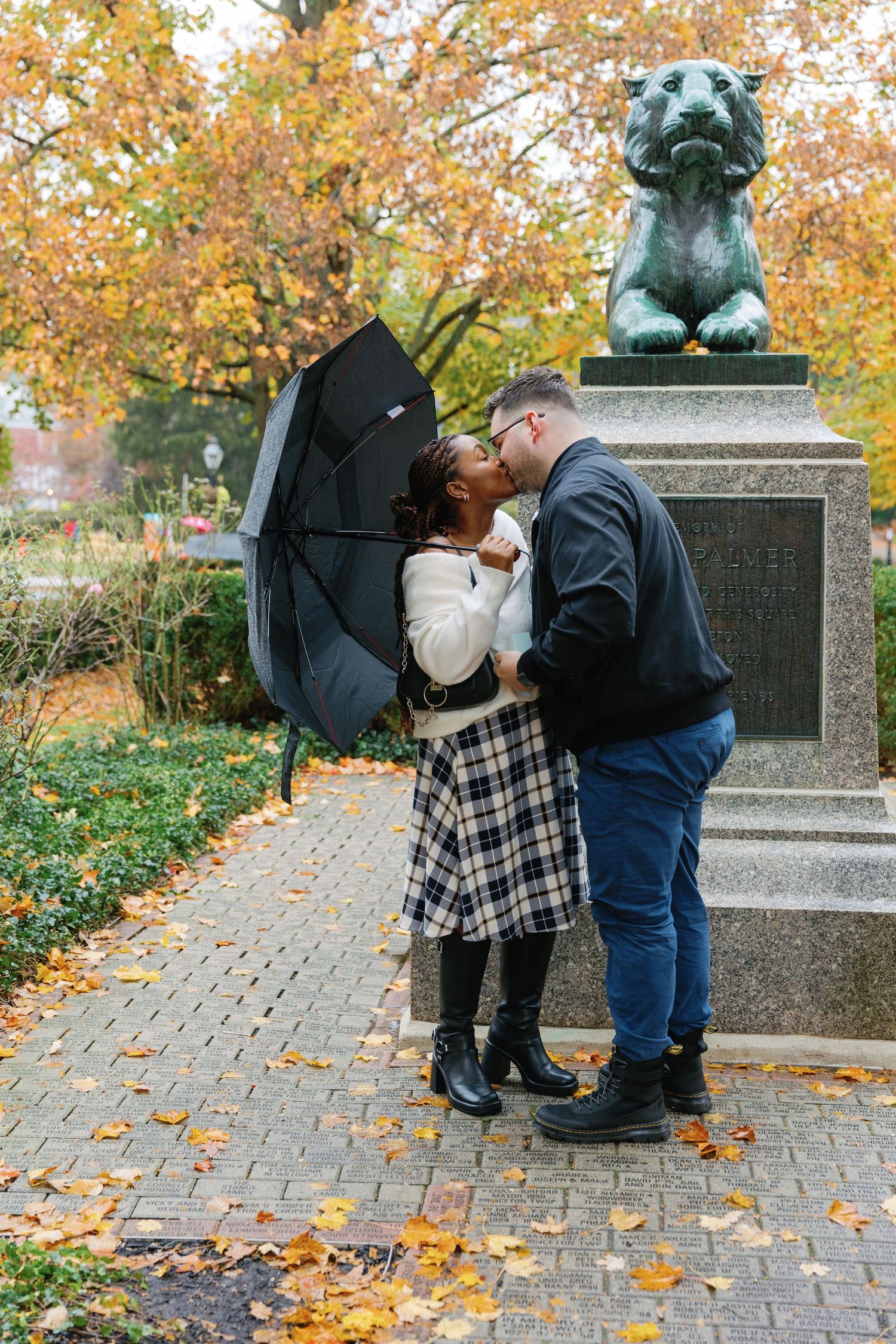 A couple shares a romantic moment near a bronze statue during autumn.