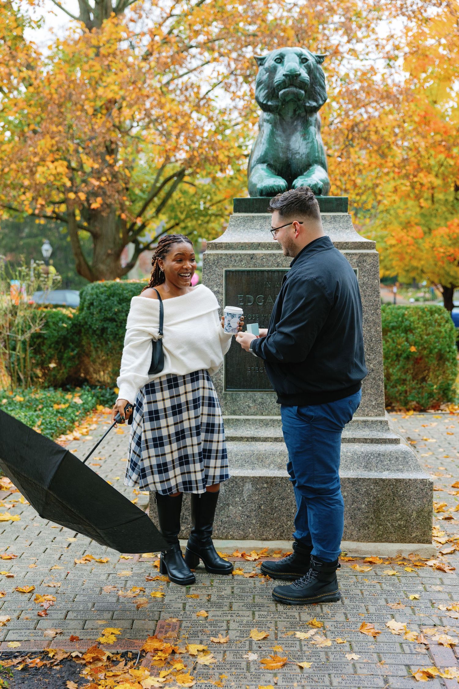 A couple shares an exciting moment by a bronze statue during autumn.