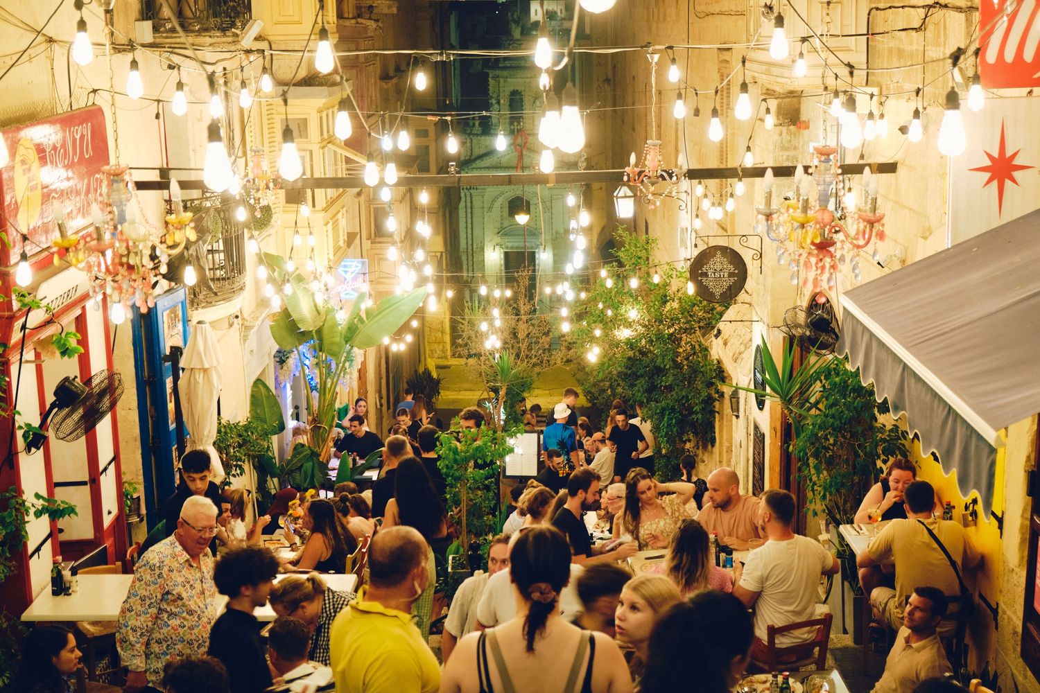 Crowded outdoor dining area illuminated by warm string lights creating a festive nighttime atmosphere.
