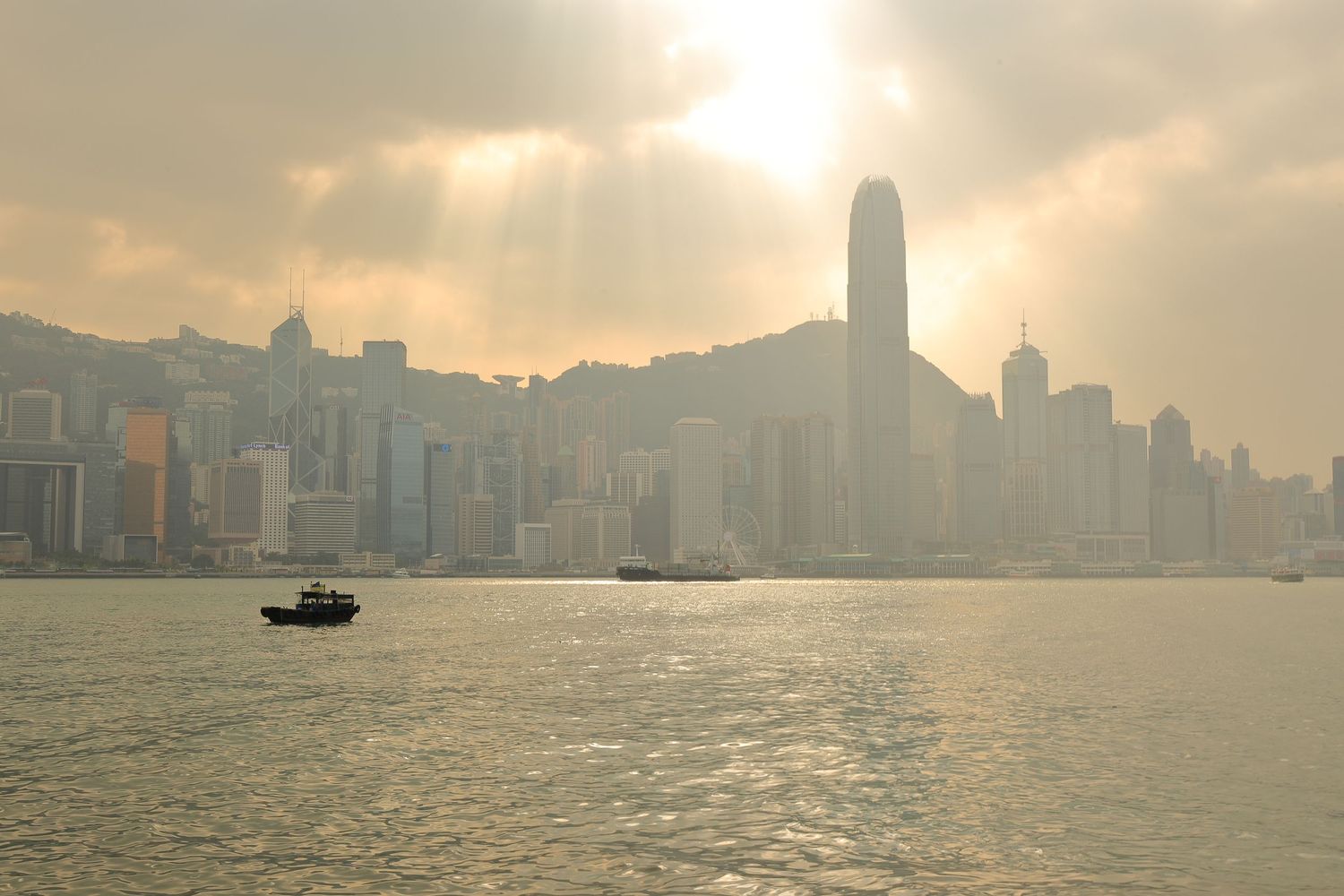 Misty Hong Kong skyline at sunset with a small boat crossing Victoria Harbour.