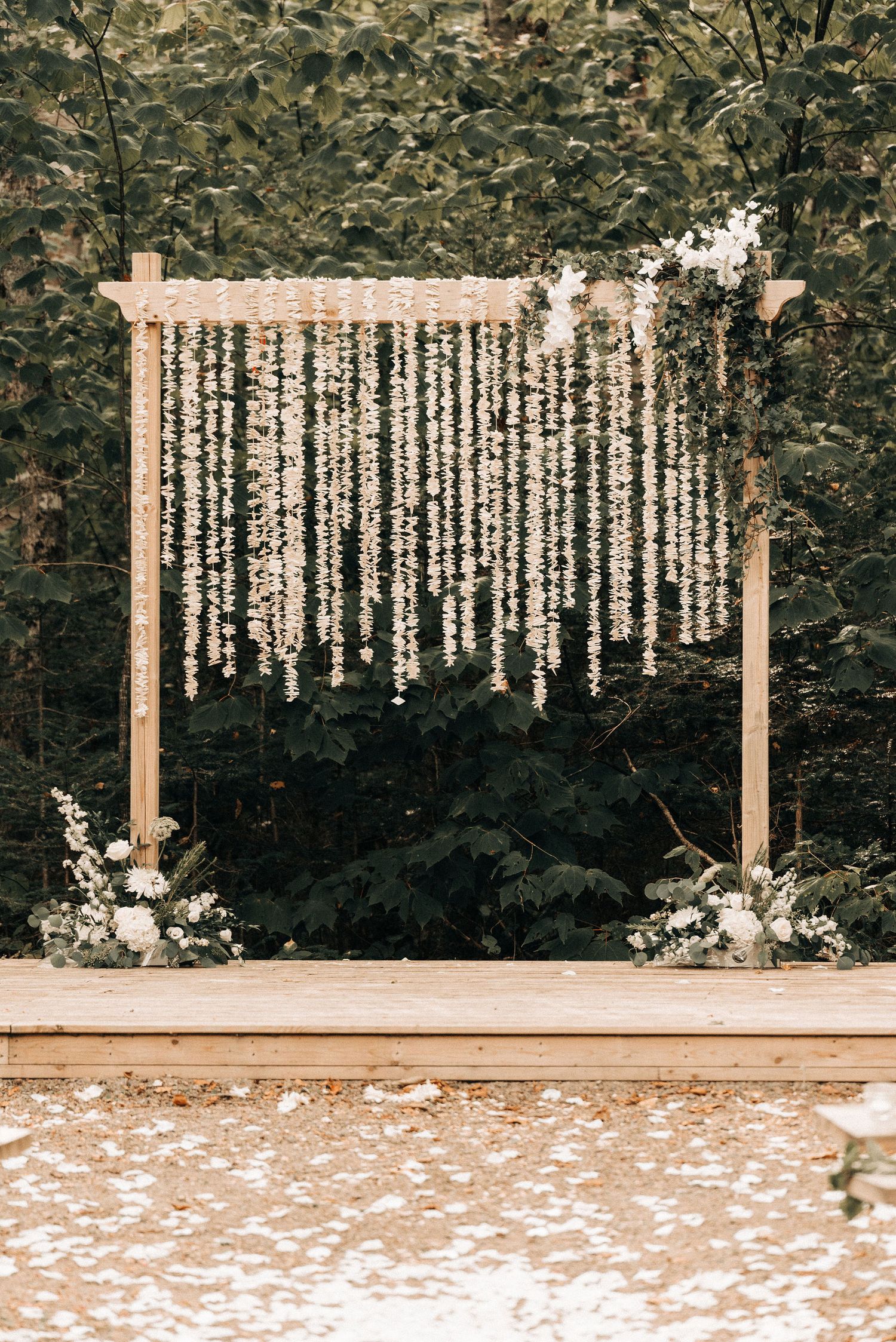 Romantic wedding arch decorated with hanging white floral strands against a natural green backdrop.