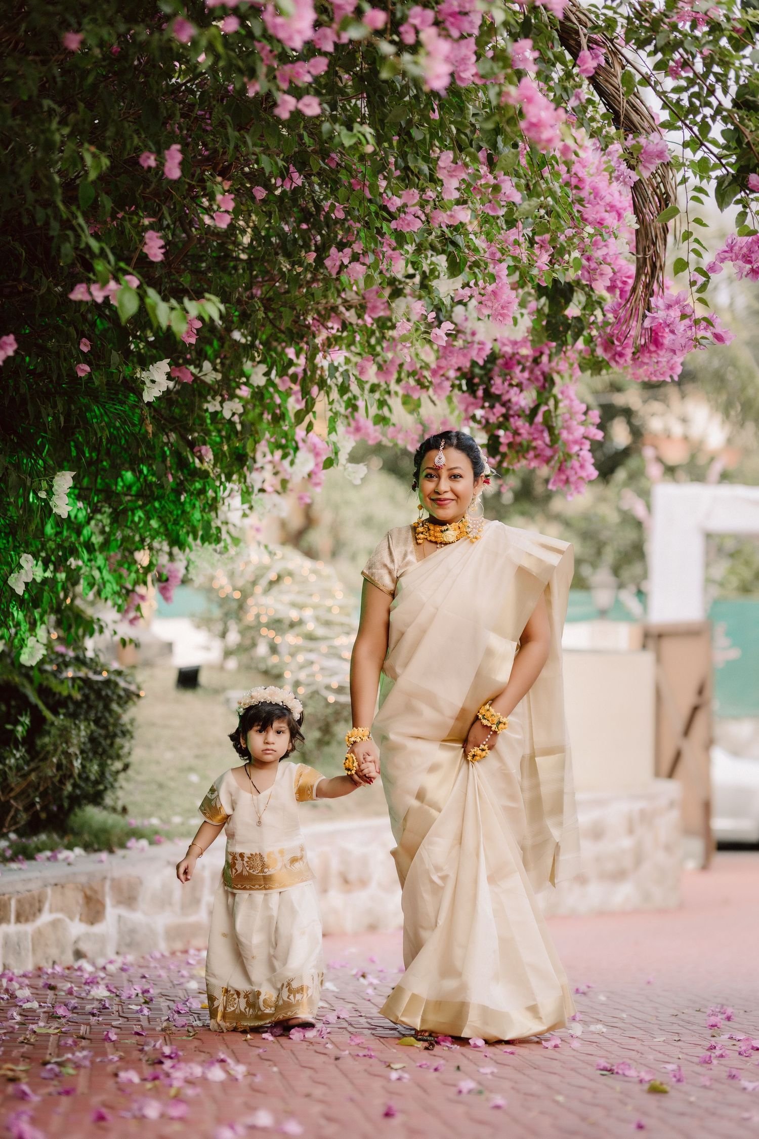 Family in cream-colored traditional Indian attire walking under pink bougainvillea flowers.