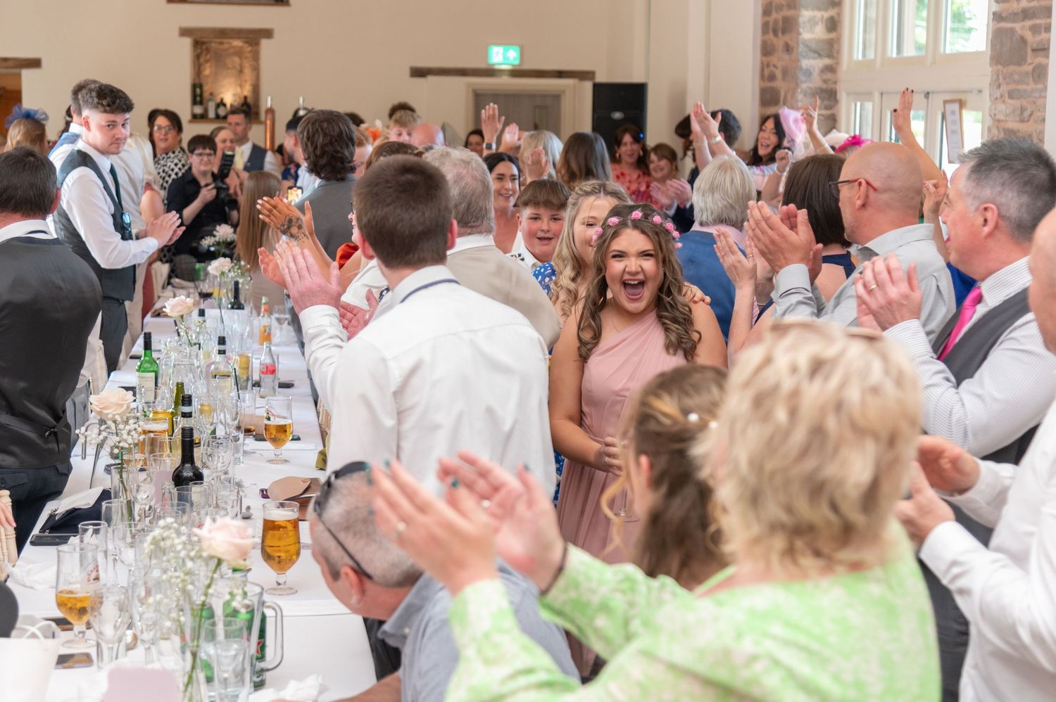 Large group of wedding guests seated at long tables during an indoor reception celebration.