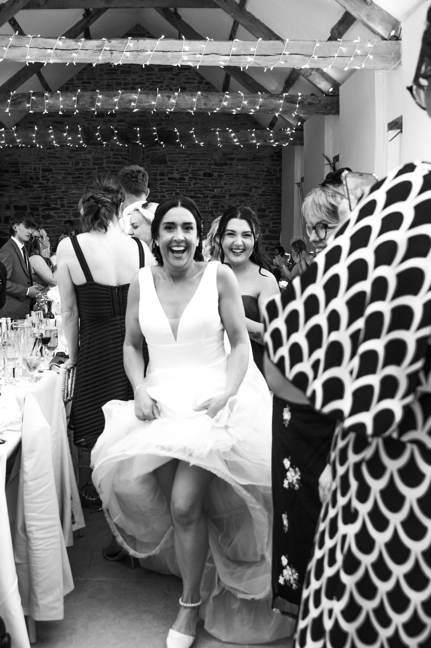Wedding party dancing and celebrating in black and white with decorative lighting overhead.