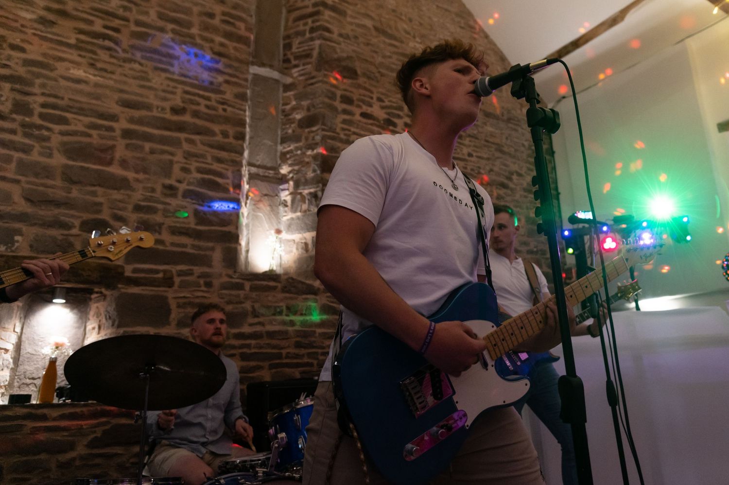 Live band performing in front of brick walls with colorful stage lighting.