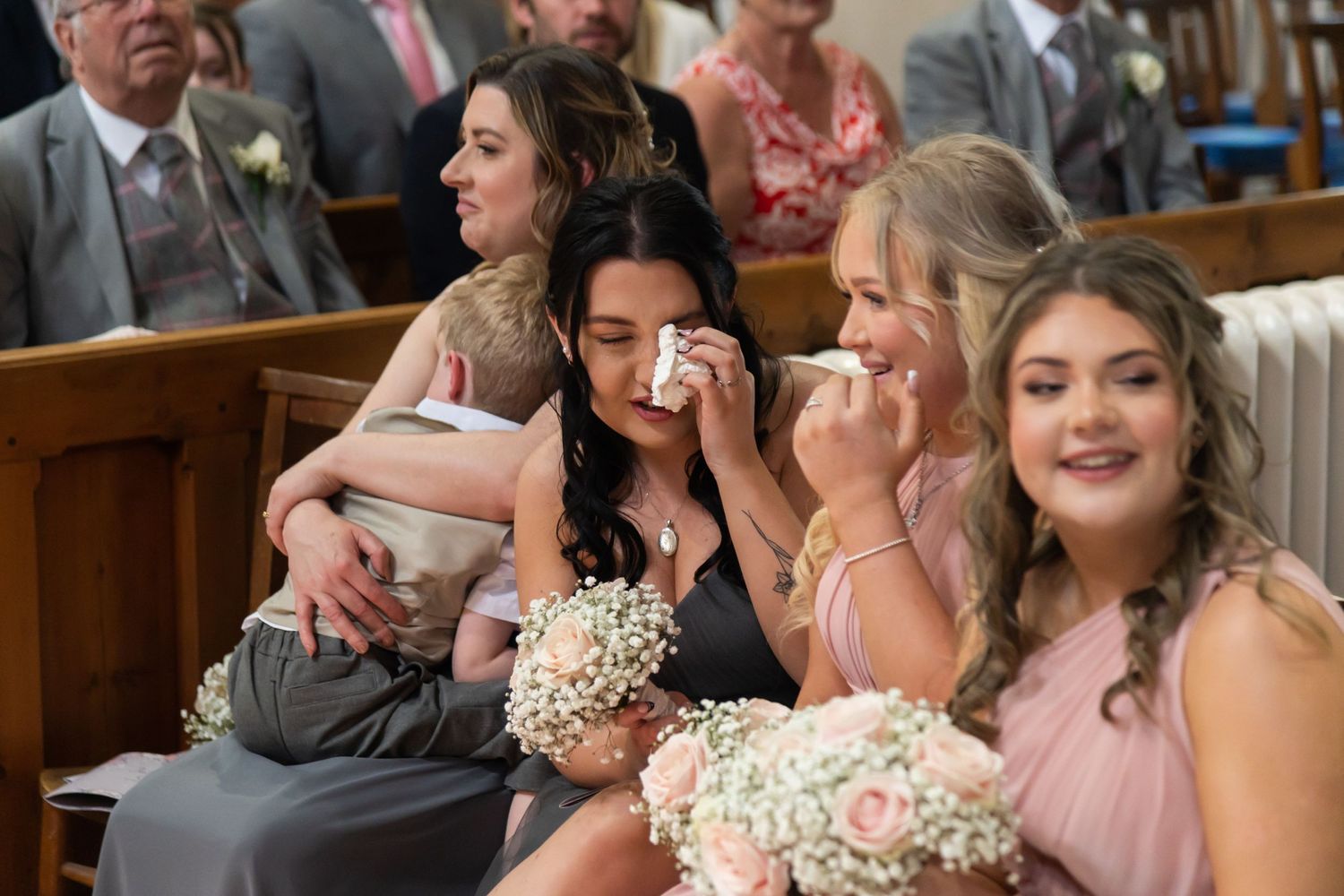 Wedding party and guests seated in church pews during emotional ceremony.