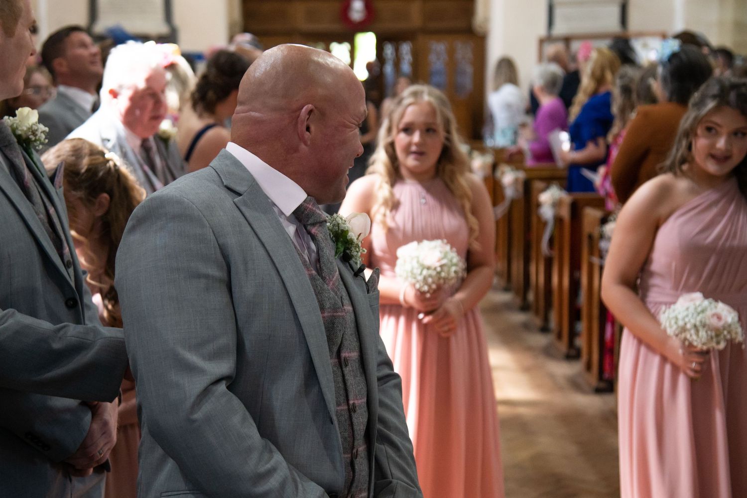 Wedding ceremony in traditional church with bridesmaids in pink dresses and groomsmen in grey suits.