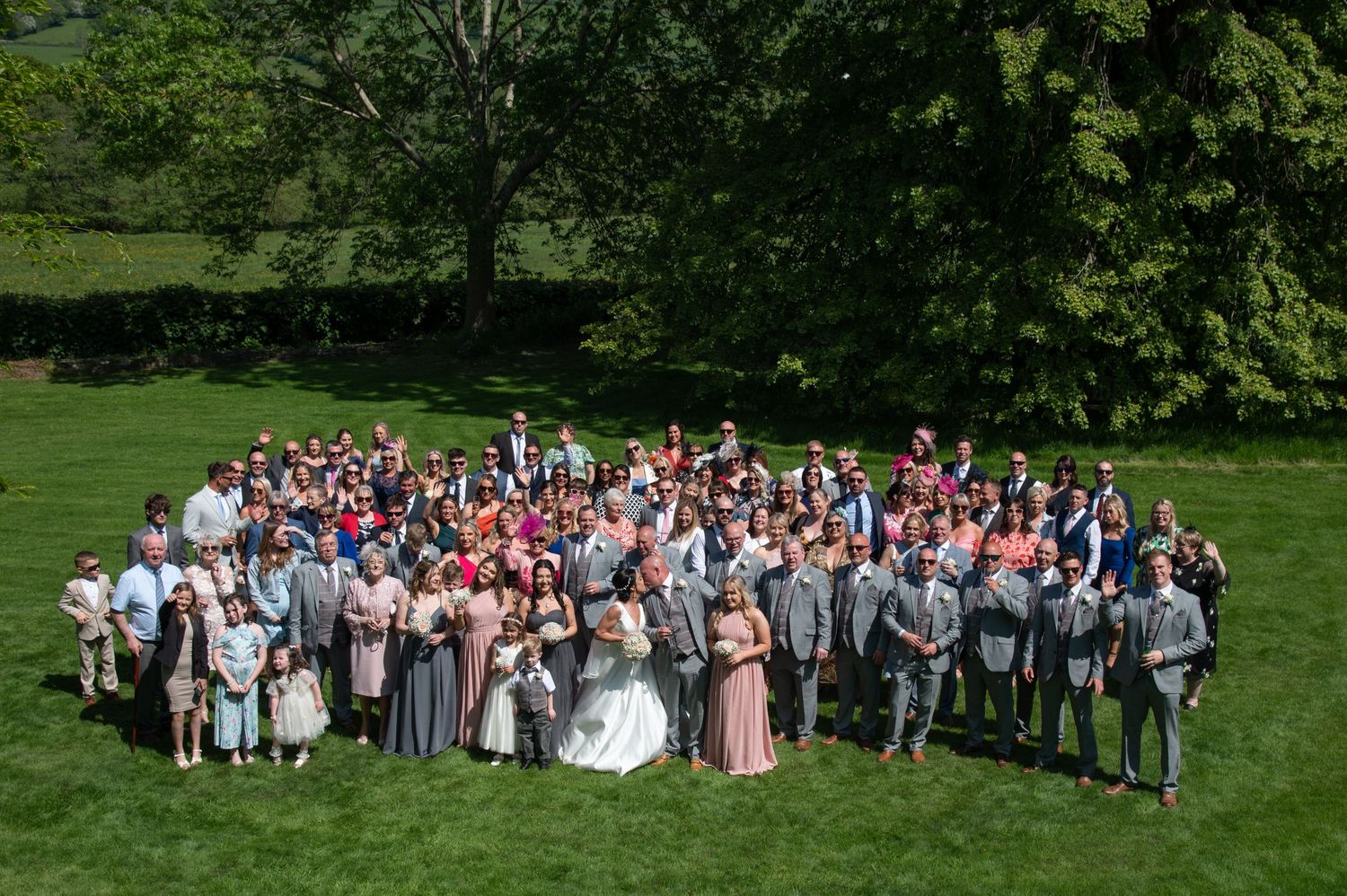 Large group wedding photo taken outdoors with green landscape background.