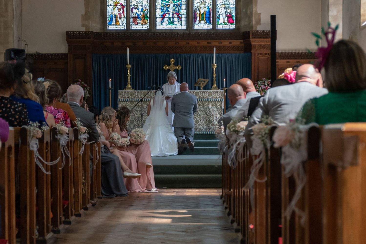Church interior with stained glass windows and wooden pews during a wedding ceremony.