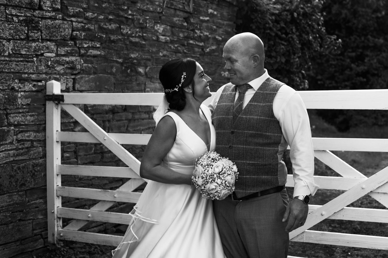 Romantic moments captured between two people near a rustic wooden gate and brick wall.