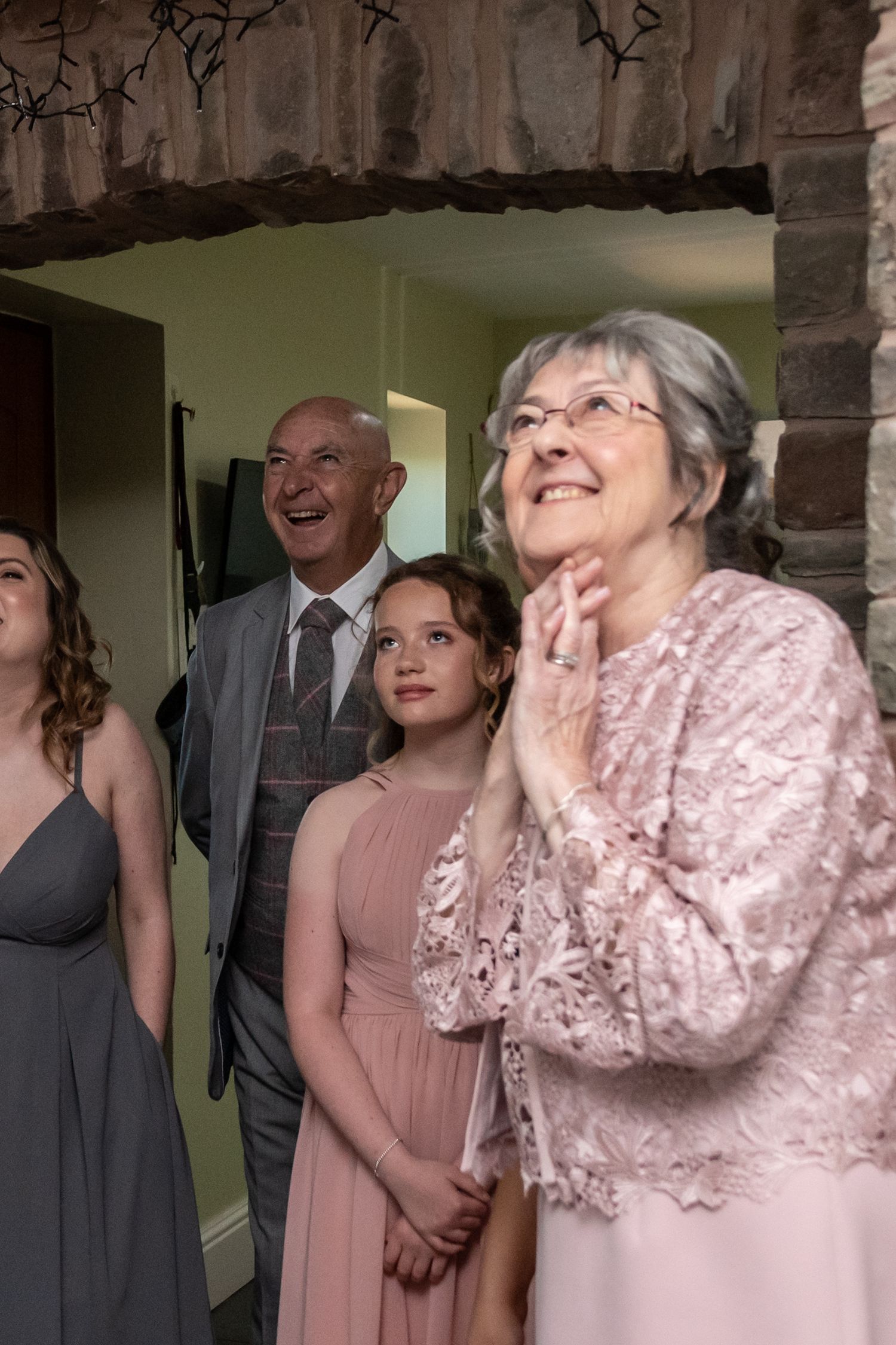 Wedding party members in pink dresses and grey suits share genuine laughter during celebration.