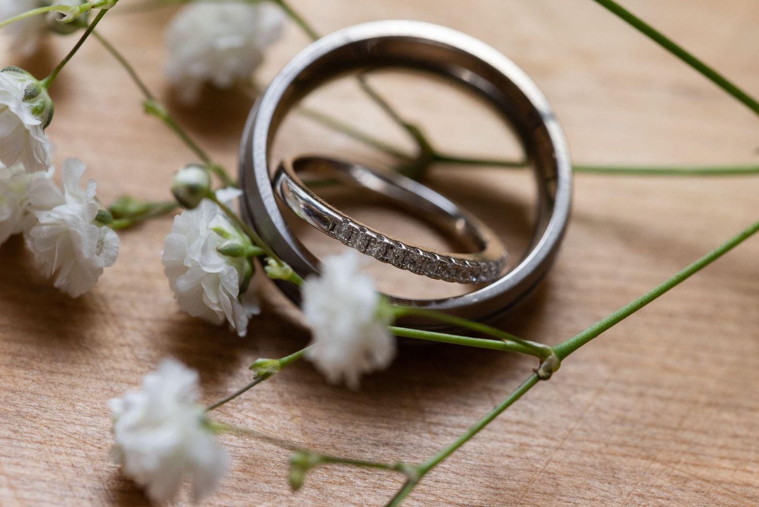 Wedding rings photographed with delicate white flowers on wooden surface.