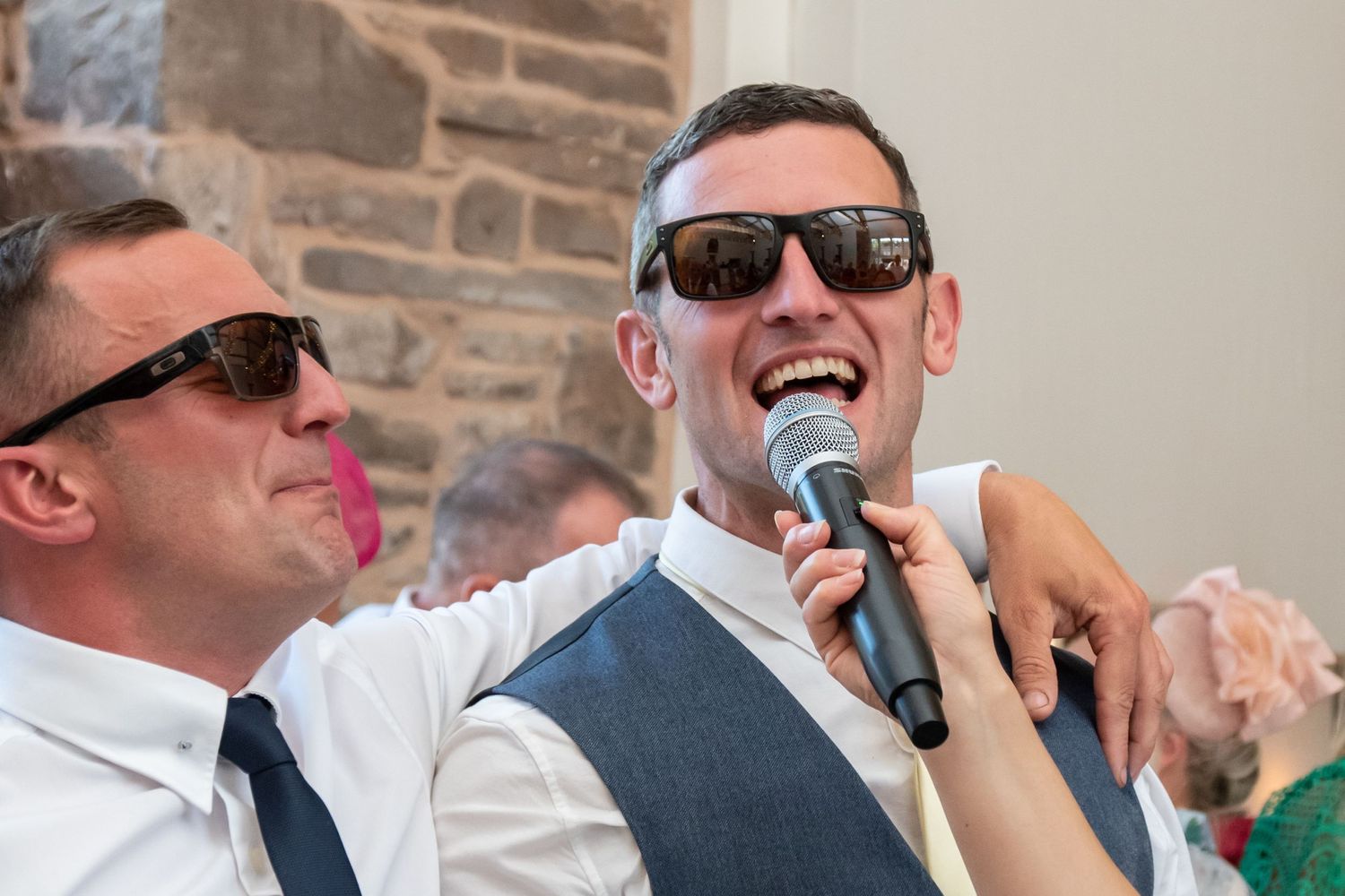 Wedding guests wearing sunglasses smile and celebrate at an outdoor reception.