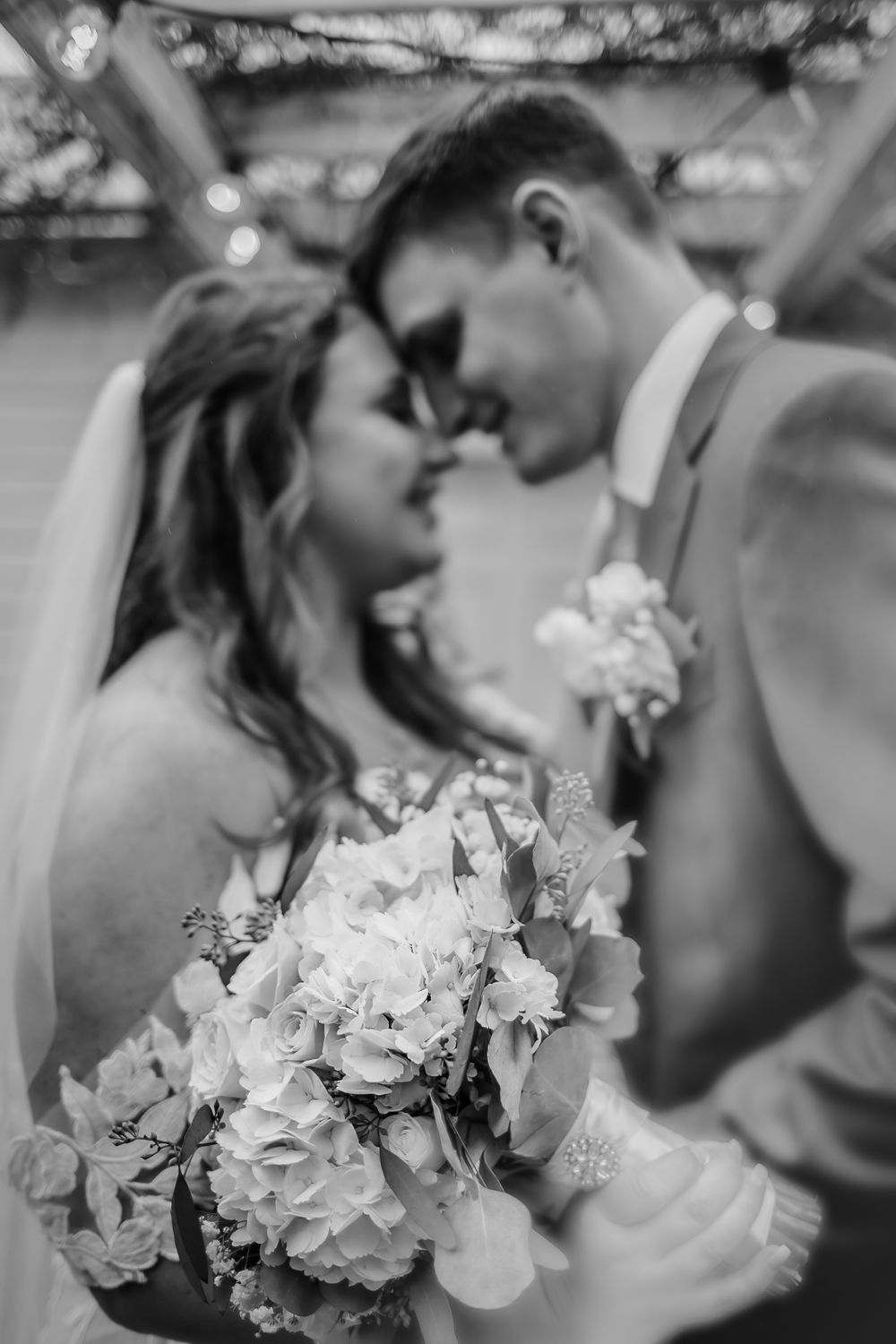 Black and white close-up of a bridal bouquet with hydrangeas as newlyweds share an intimate moment.