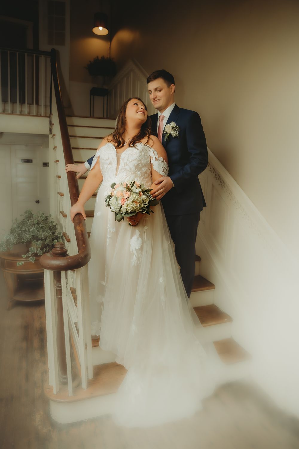 Newlyweds pose on an elegant staircase with bride holding a romantic floral bouquet.