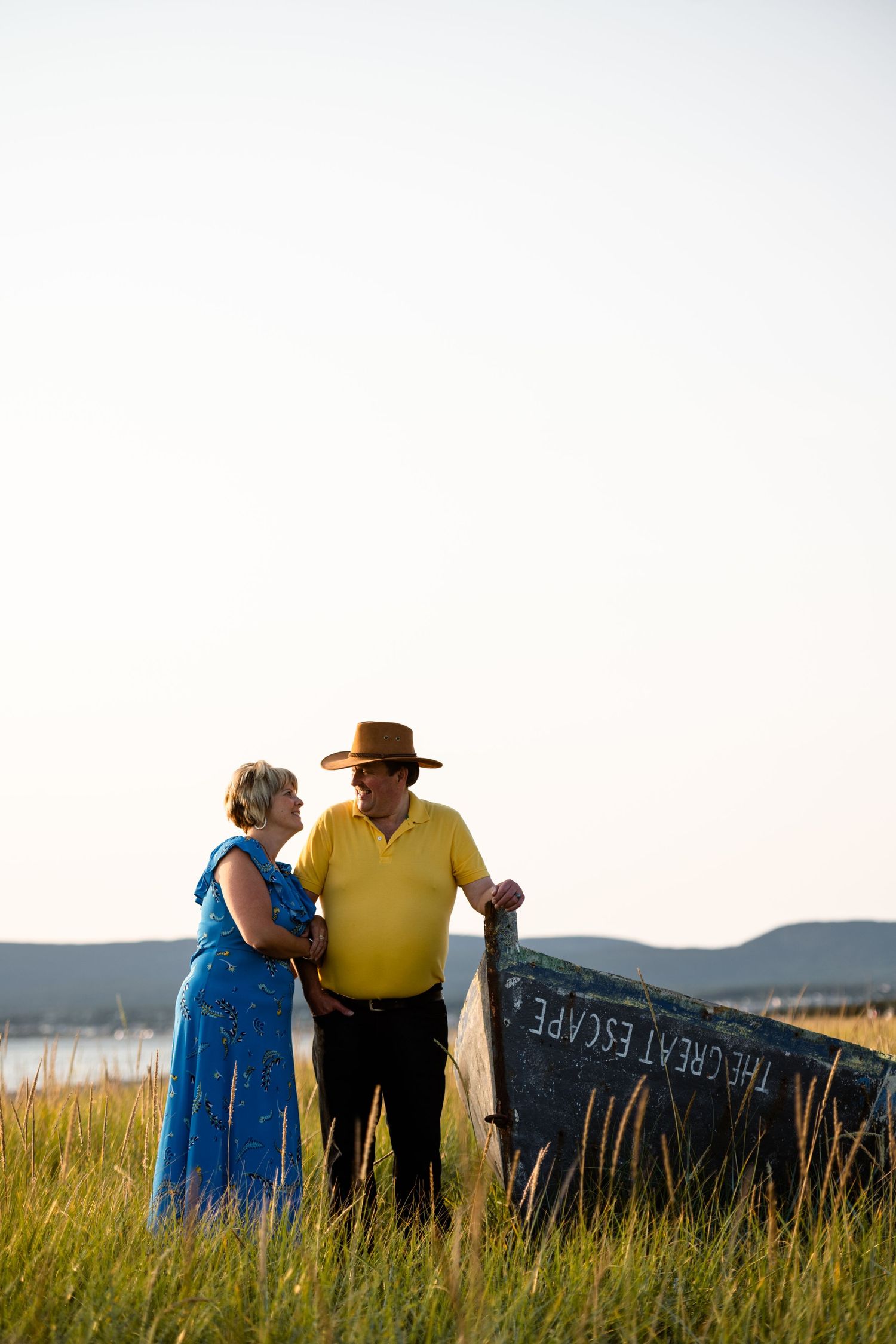 Couple standing in field at sunset next to rustic wooden sign.