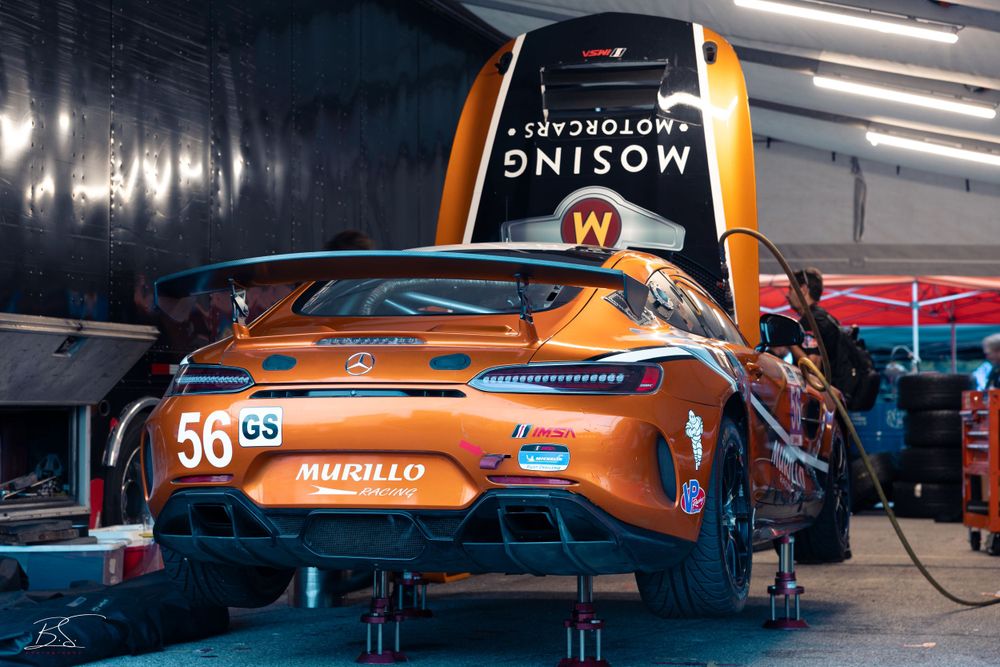 An orange Mercedes-AMG GT race car number 56 in a pit garage with Woking Motorcars branding.
