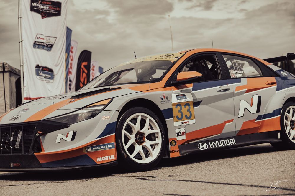 A Hyundai Elantra N TCR race car number 33 with orange and silver livery parked at a racing event.