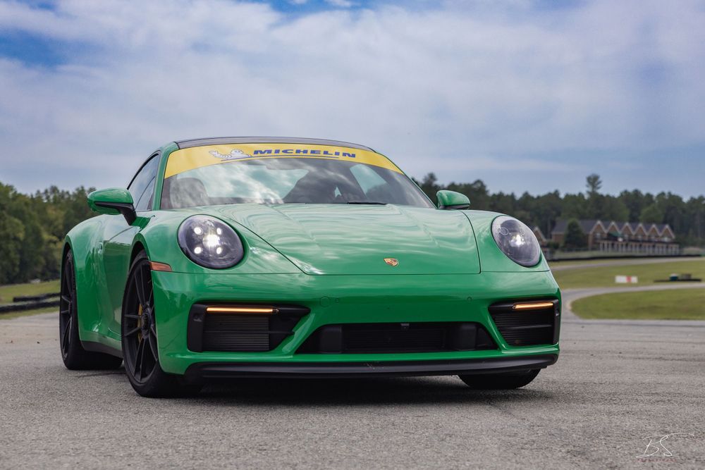 A vibrant green Porsche 911 Carrera on a race track with Michelin branding on the windshield.