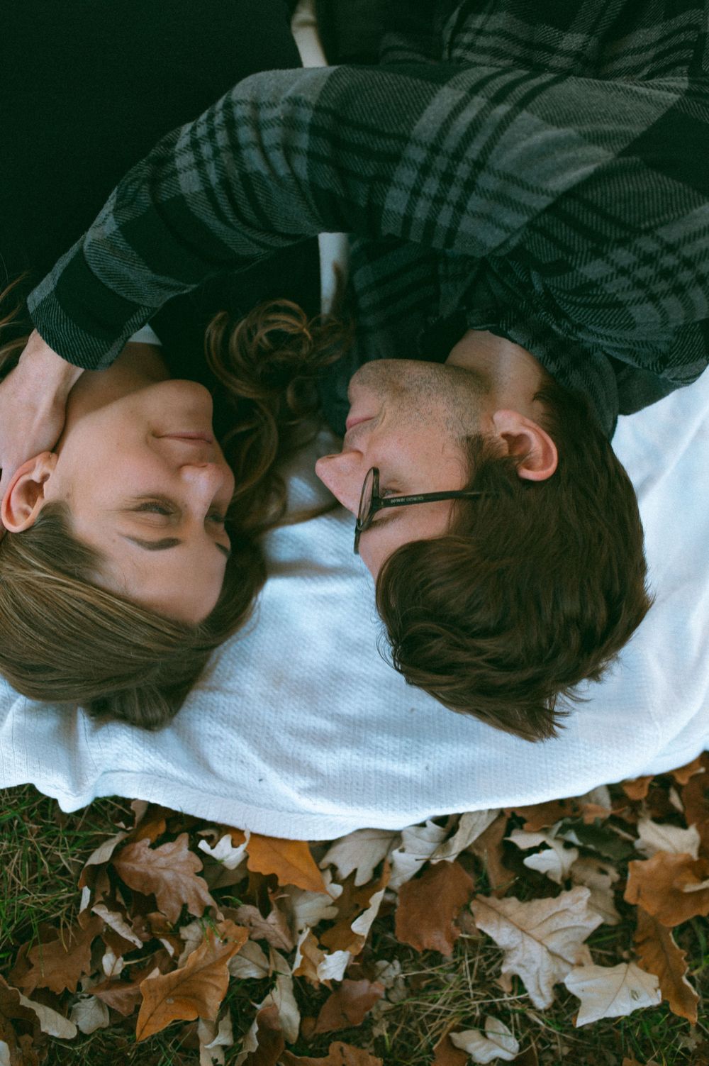 Overhead view of couple lying on white blanket surrounded by autumn leaves.