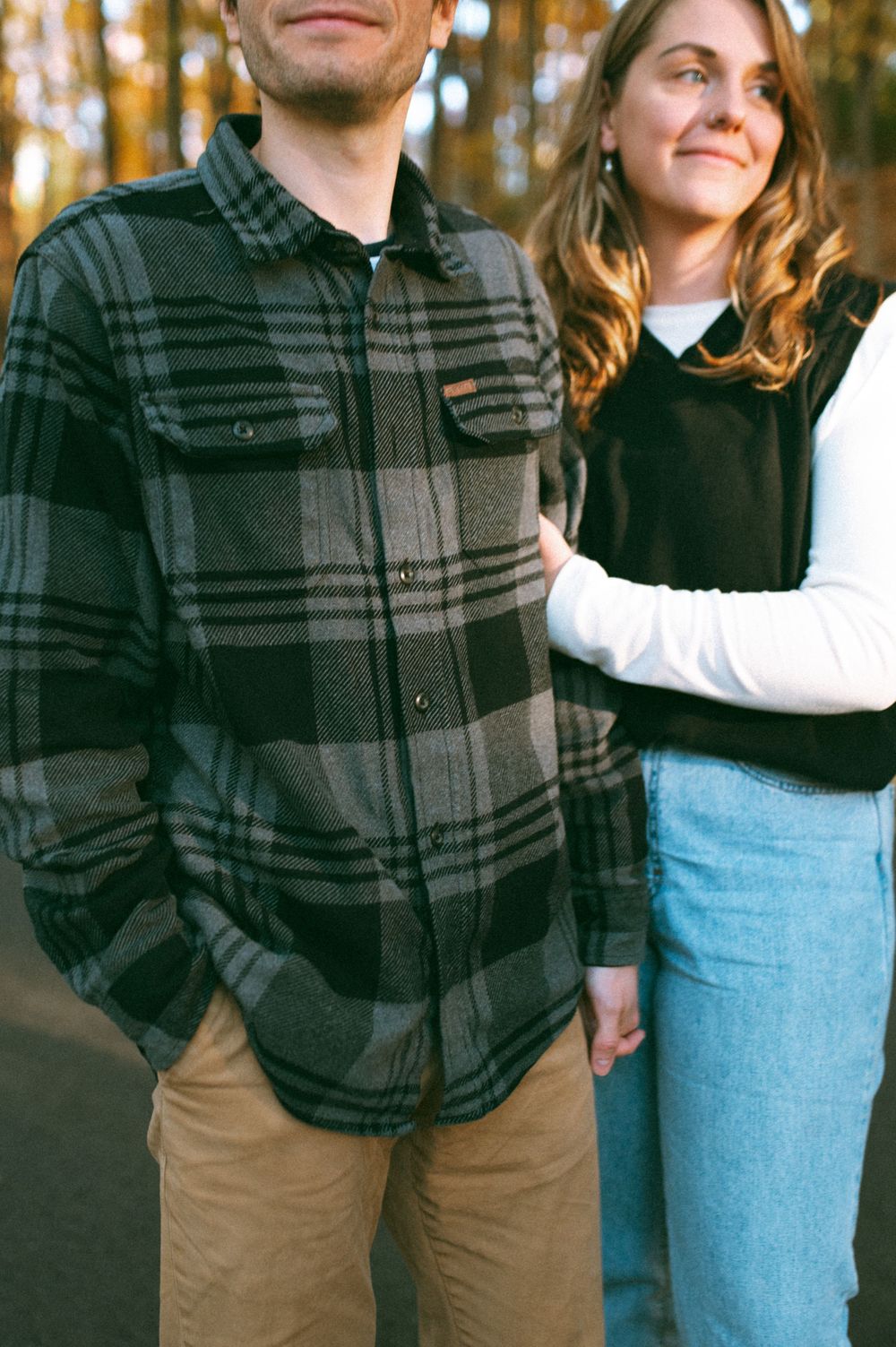 Casual couple in plaid and denim stands together in autumn forest setting.