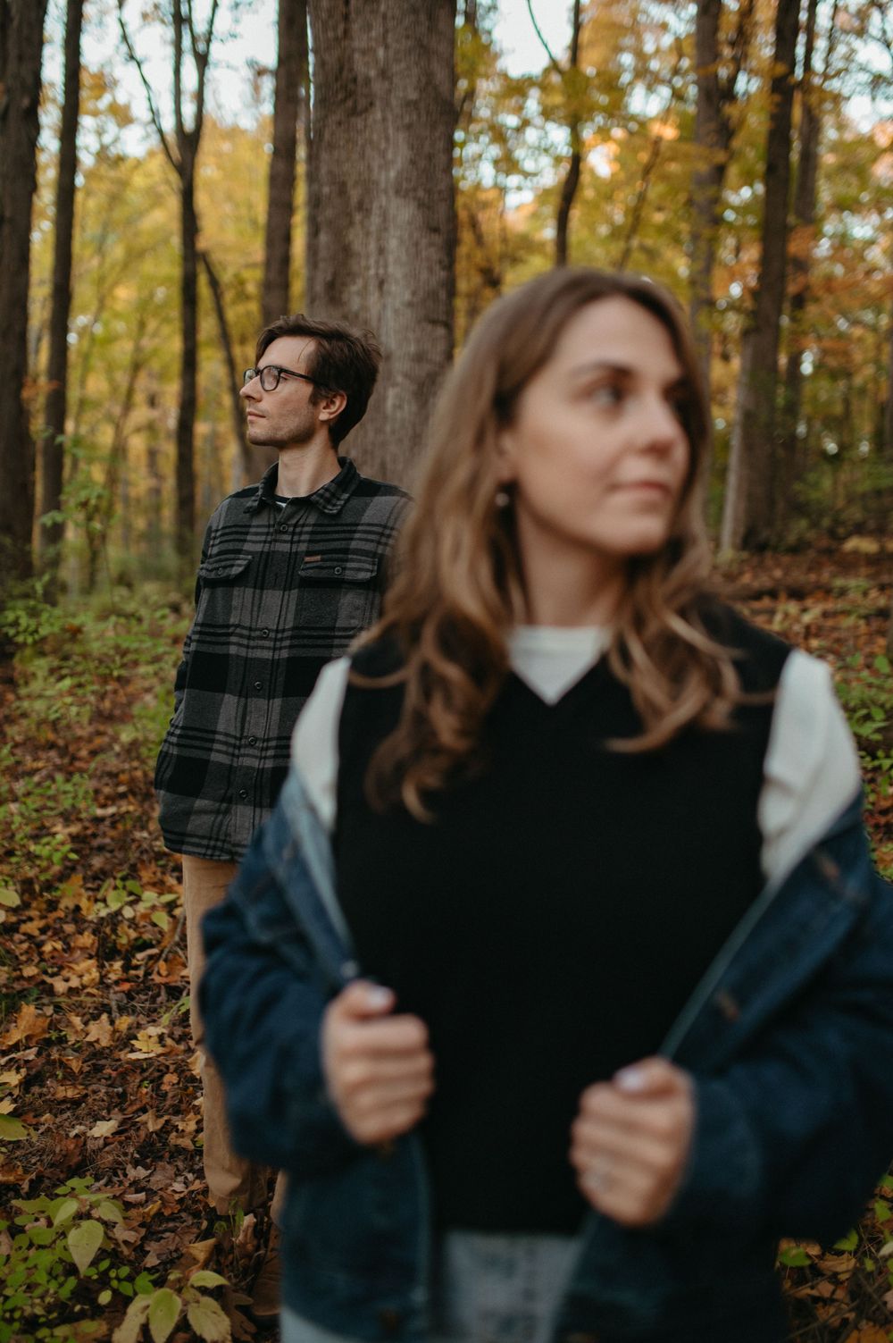 Artistic autumn portrait of two people standing separated between trees with golden leaves.