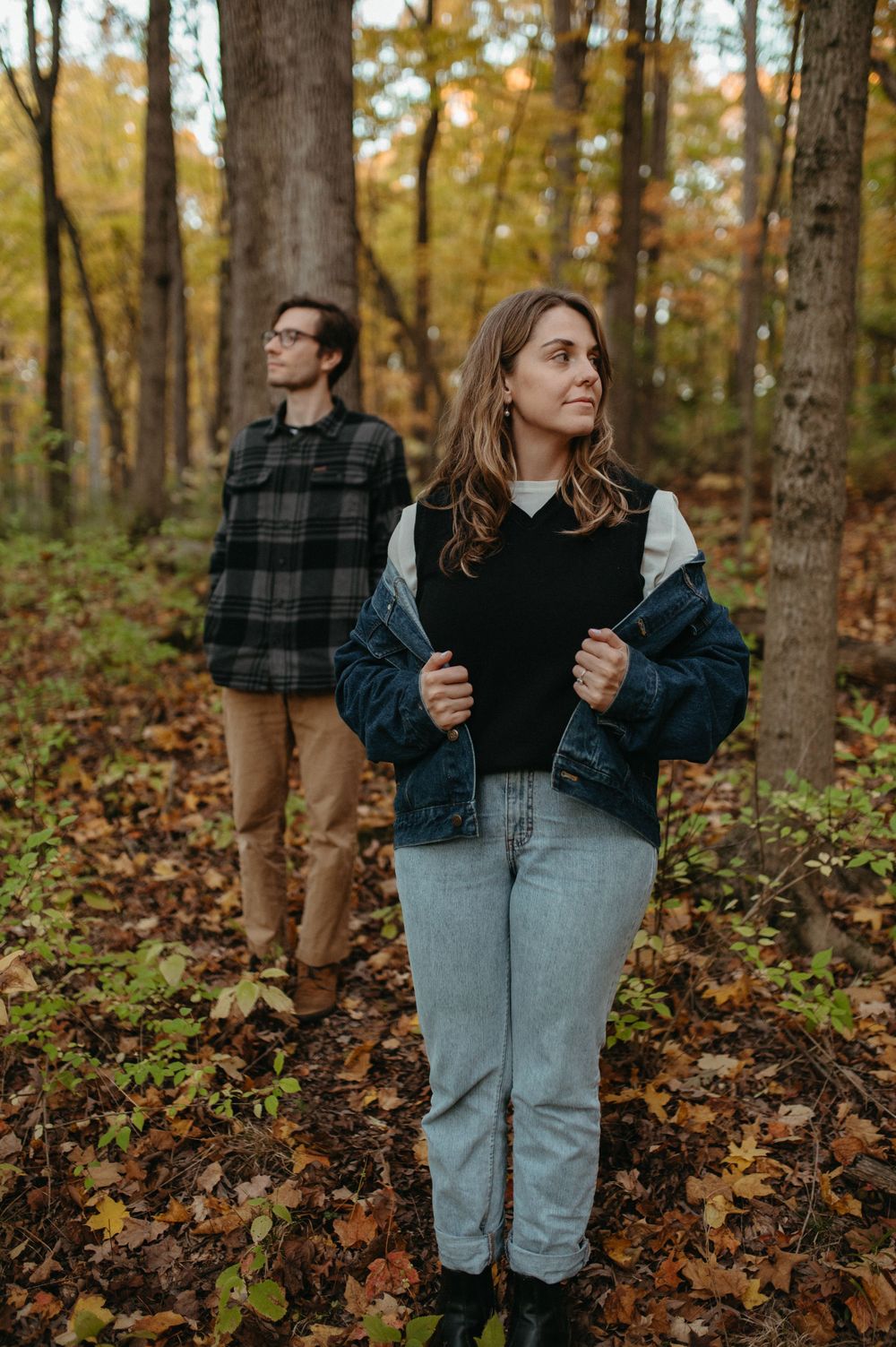 Two people standing in an autumn forest wearing casual fall clothing and denim.