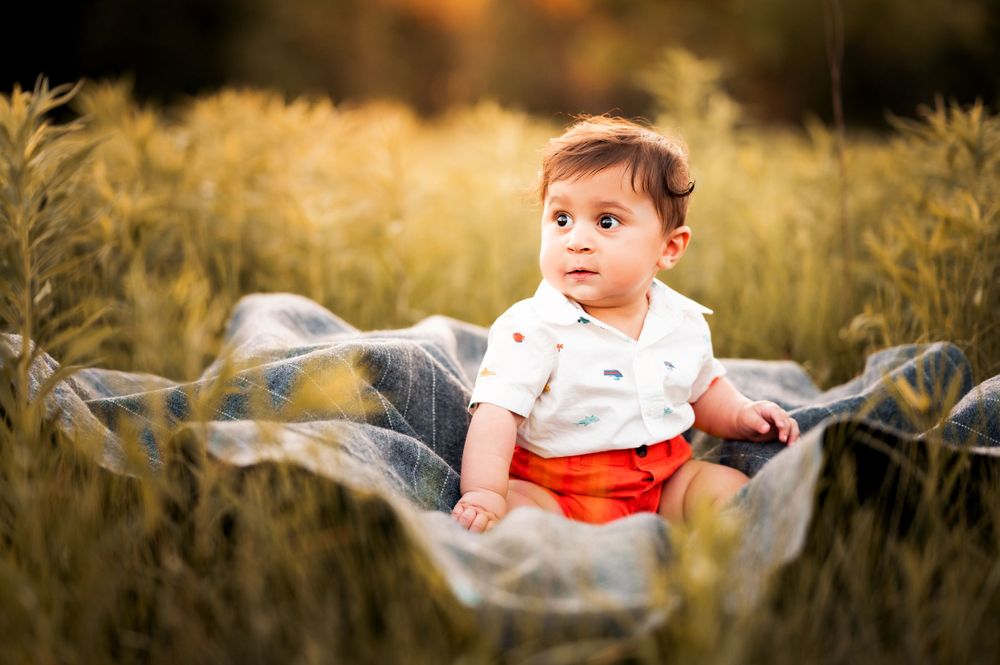 Baby sits on blanket in tall grass during golden hour outdoor photoshoot.