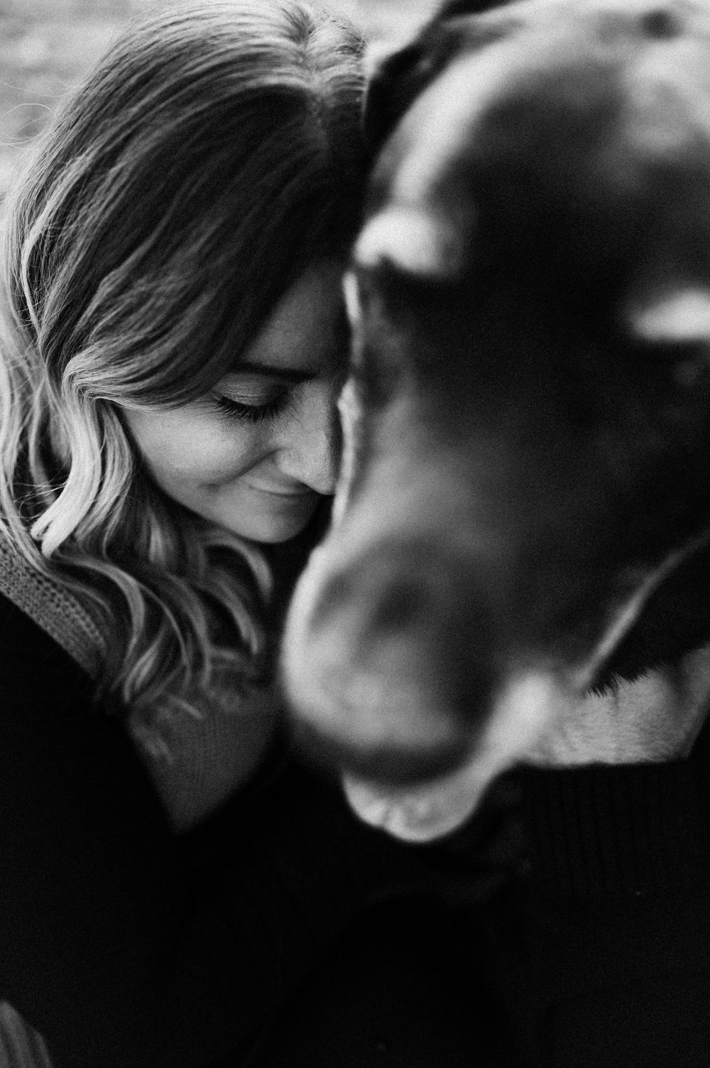 Black and white close-up of woman sharing a tender moment with her dog.