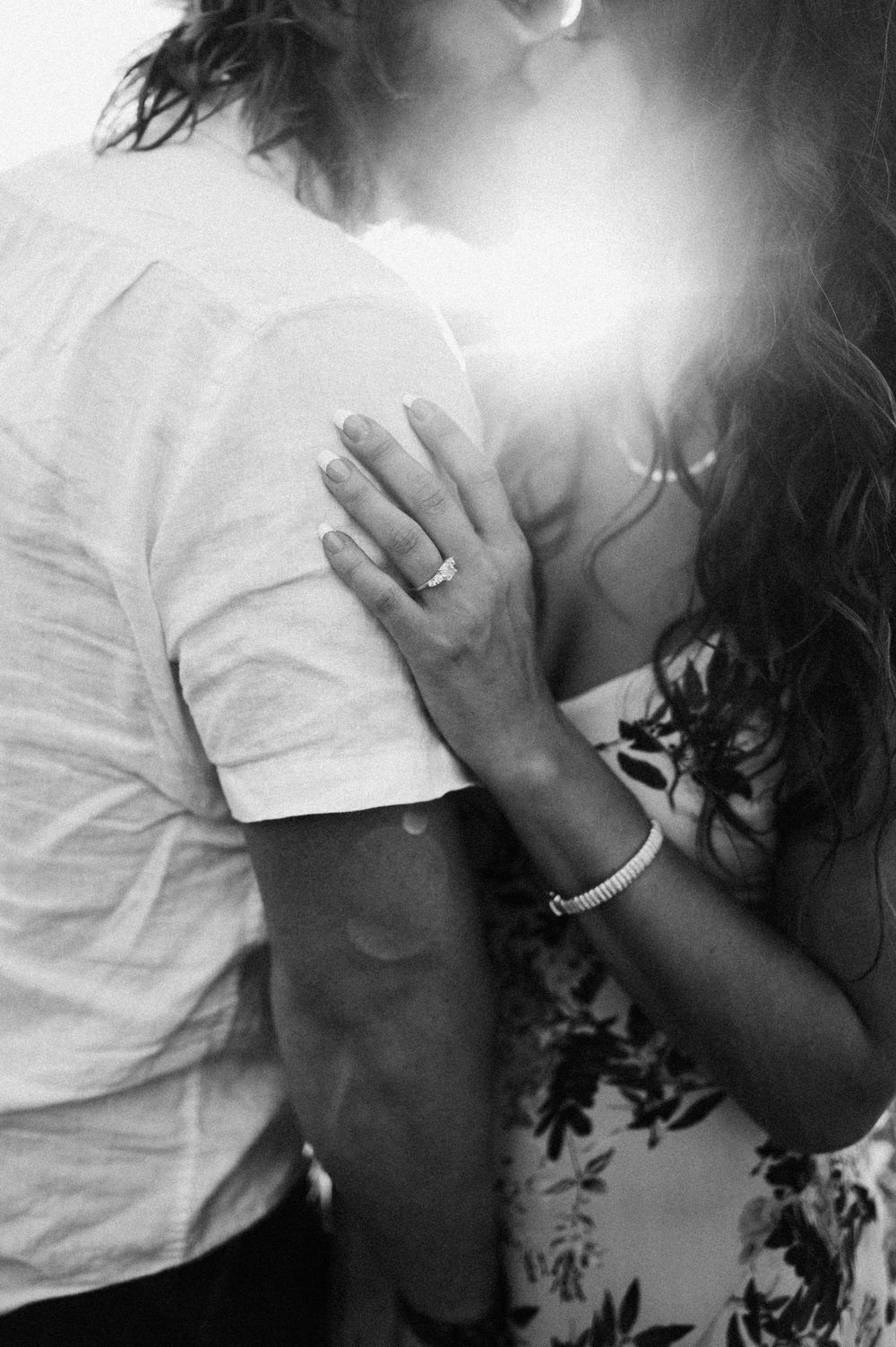 Black and white intimate portrait of couple embracing with sunlight between them.