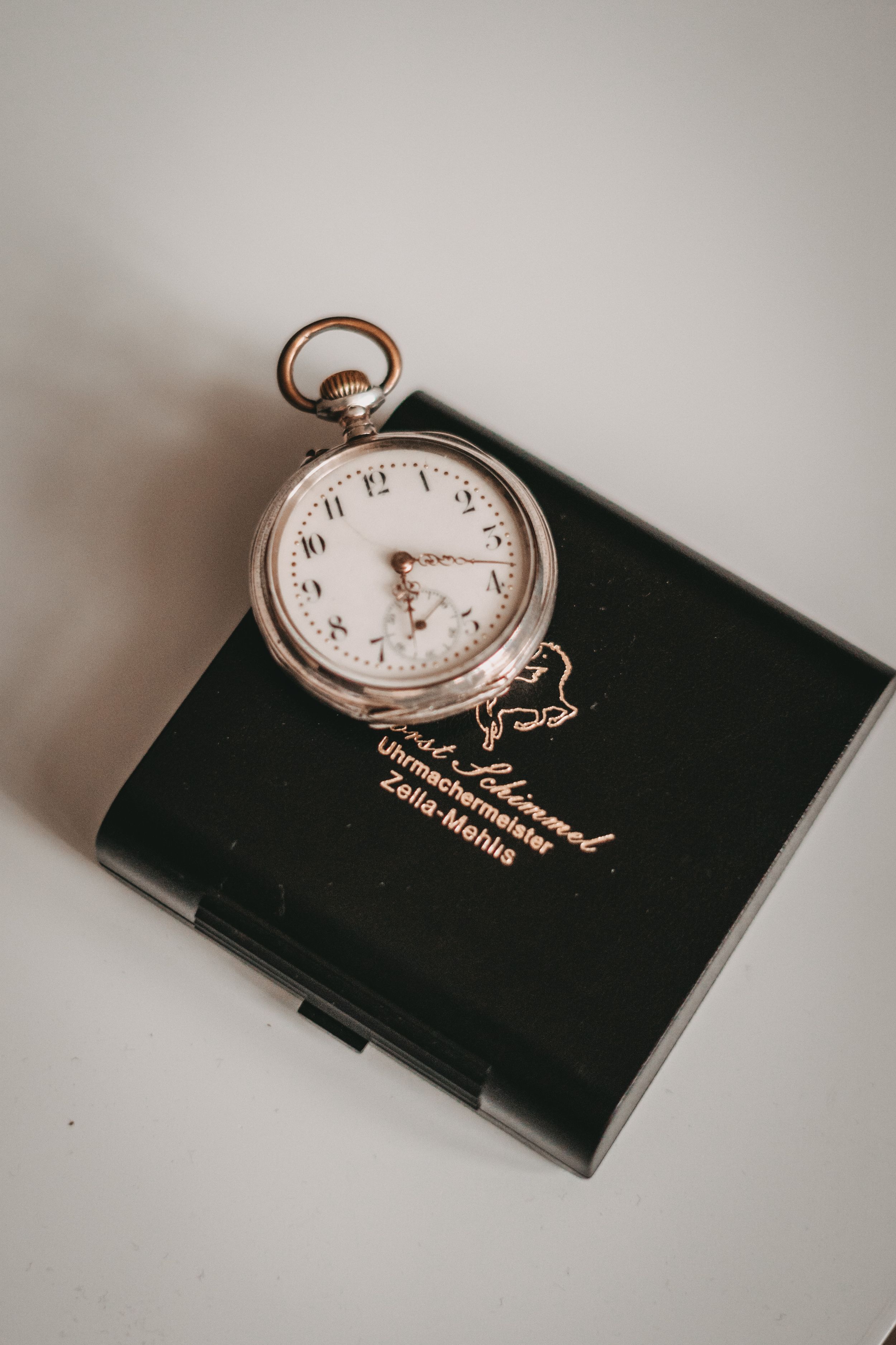 Antique pocket watch displayed on dark leather box with gold lettering.