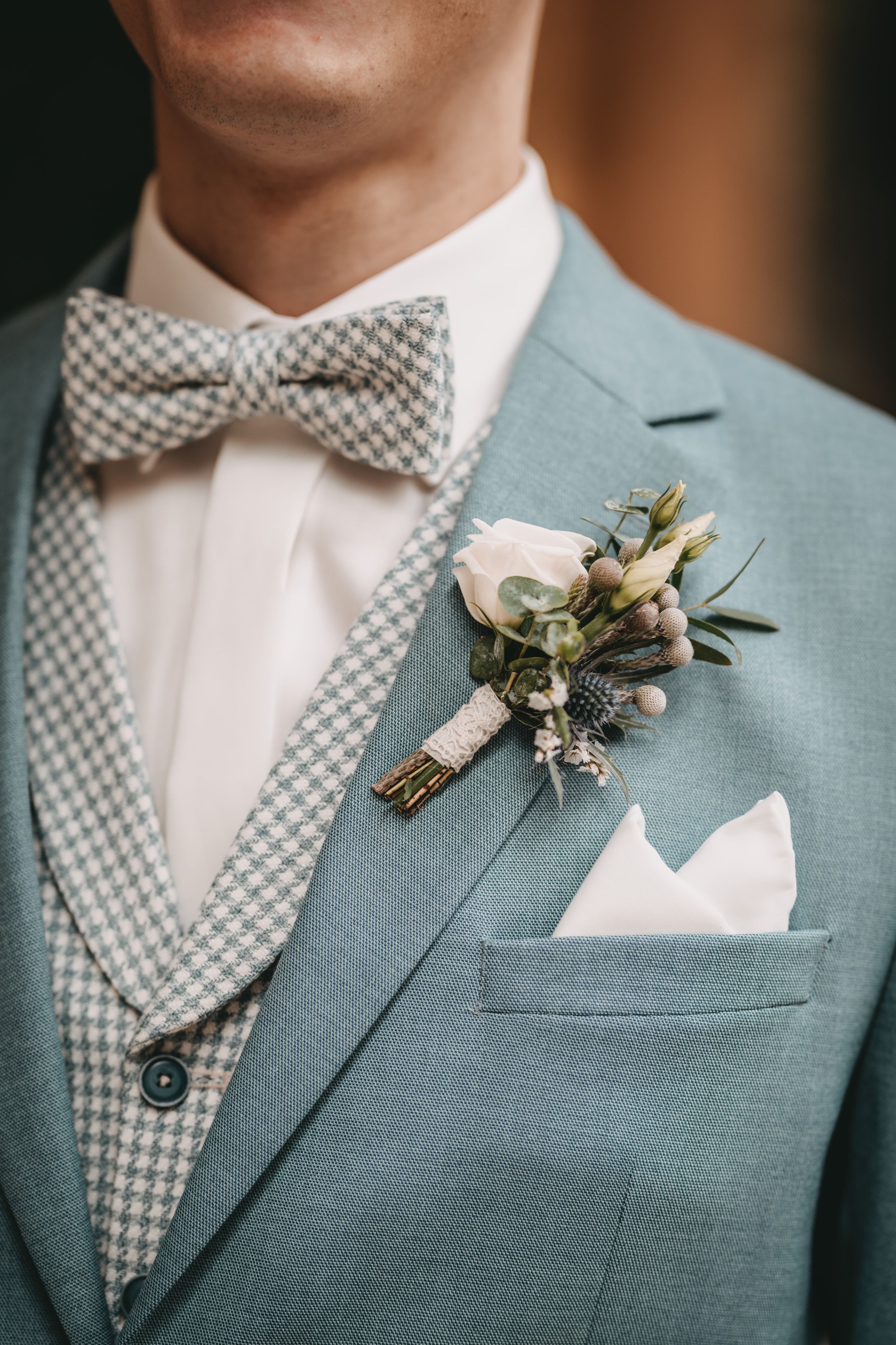 Detail of groom's sage green suit with checkered bowtie and white floral boutonniere.