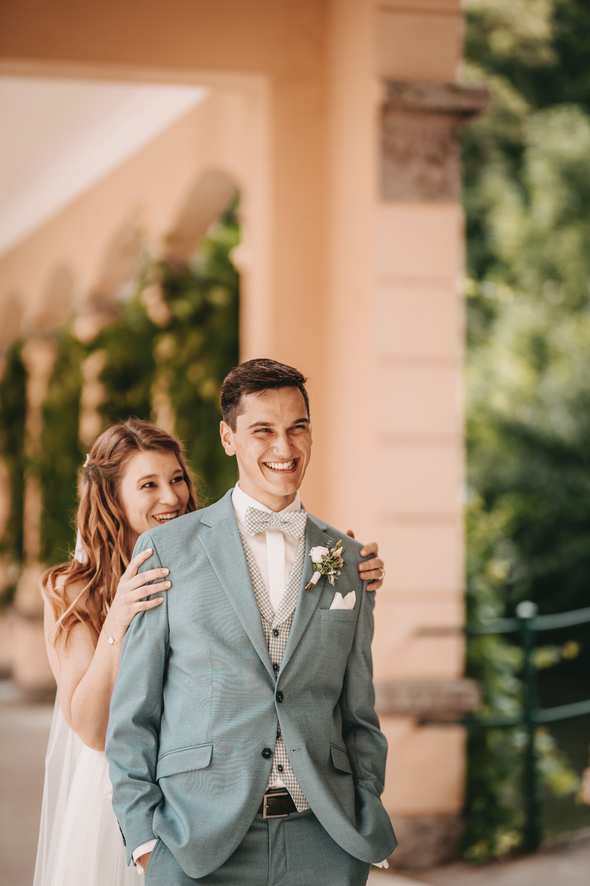 Wedding first look moment in a columned walkway with bride in white and groom in sage suit.