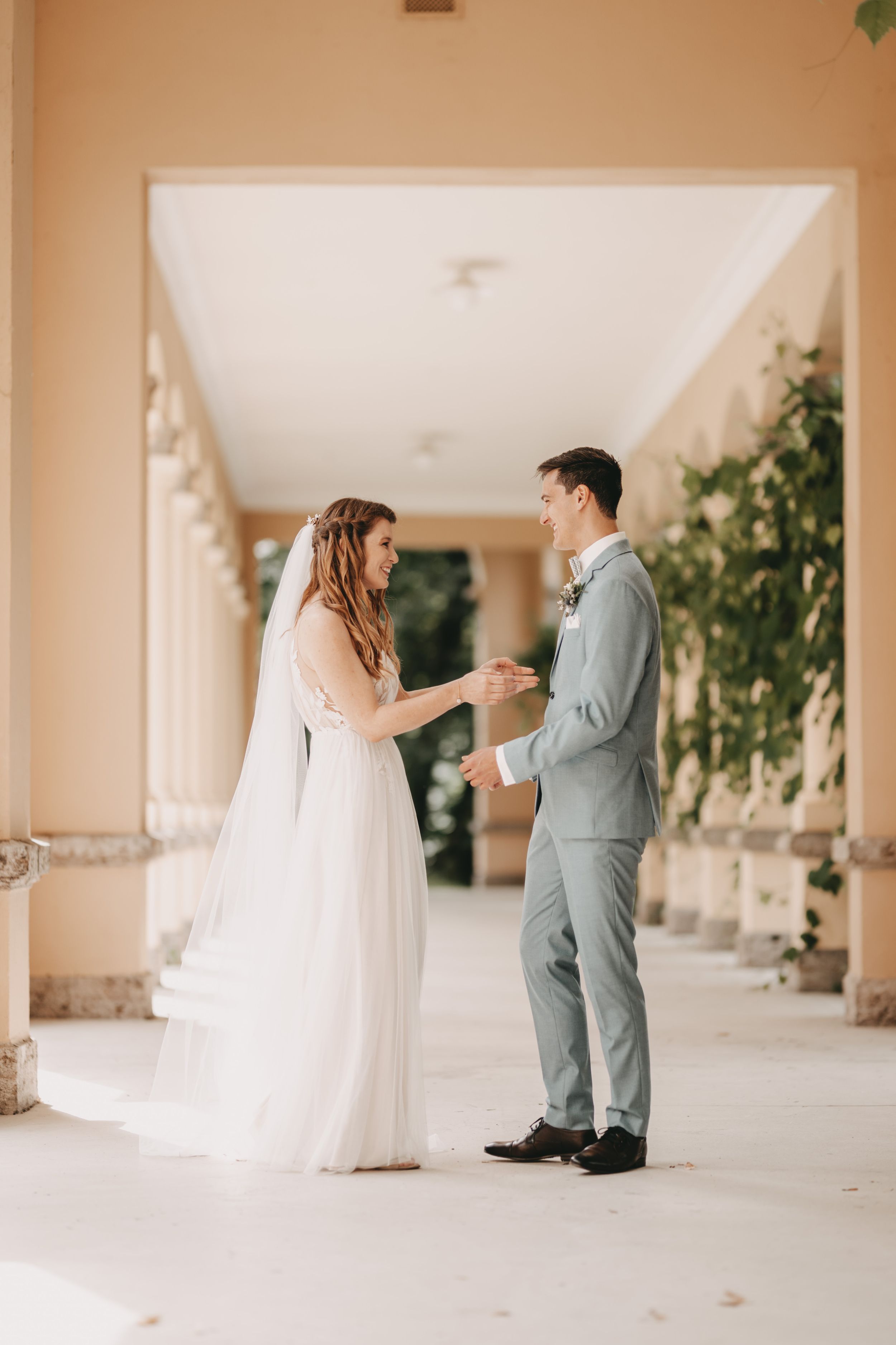 Wedding couple sharing a sweet moment in a sunlit colonnade.
